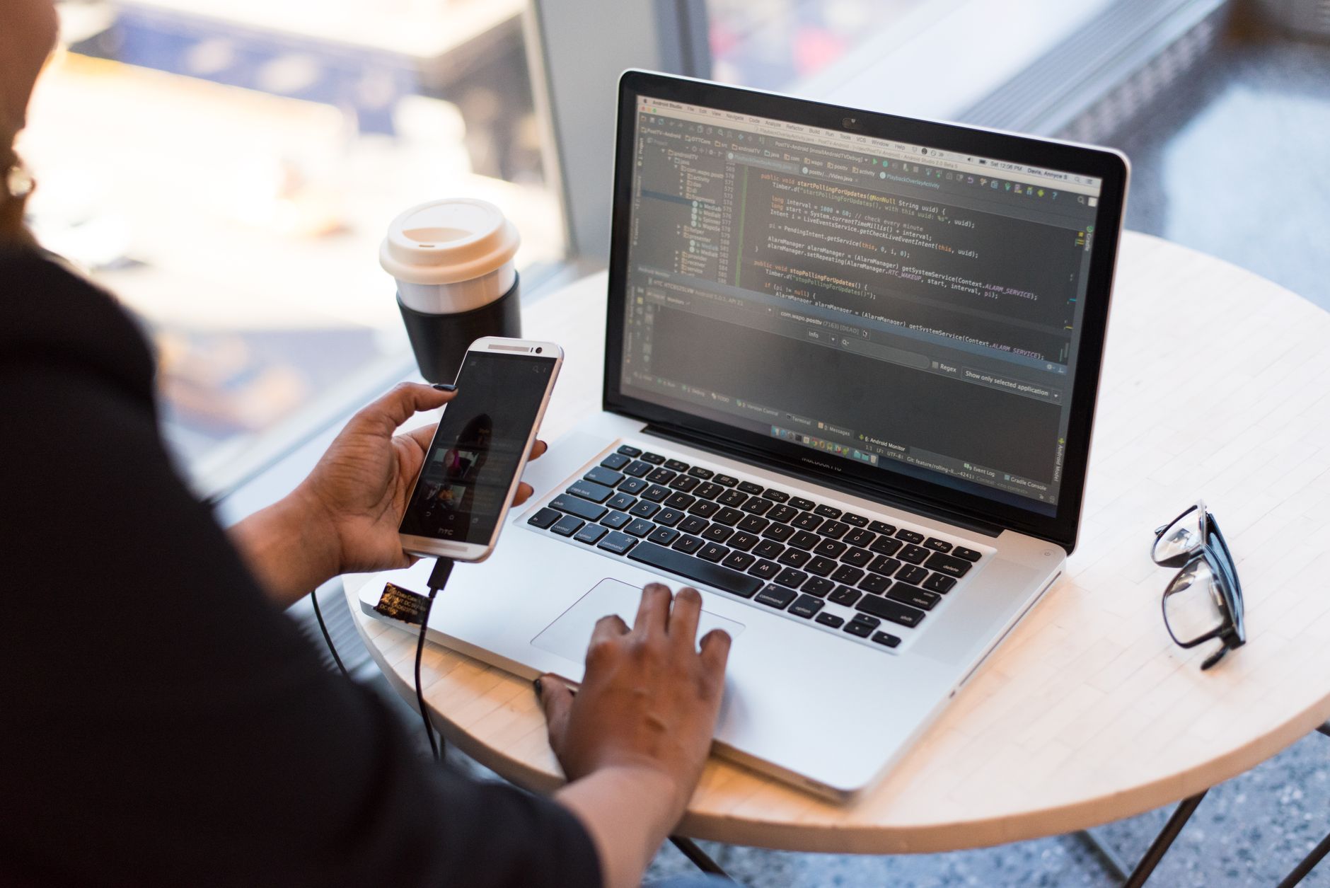 Une personne utilisant un ordinateur portable affichant du code tout en tenant un smartphone relié par un câble.